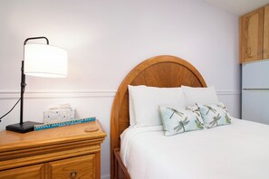A neatly made bed with a wooden headboard, a bedside lamp, a book titled "What Happens at the Beach," and a tissue box on a wooden nightstand. - Walkout Beachfront Condo: Pointes North Resort 106 (Traverse City)