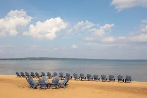 A beach with rows of Adirondack chairs facing a calm sea under a partly cloudy sky. - Walkout Beachfront Condo: Pointes North Resort 106 (Traverse City)