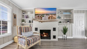 A living room with a fireplace, a striped sofa, and a large painting of a beach scene. - Sea La Vie Villa 3BD Beach Retreat Fence Yard (North Myrtle Beach)