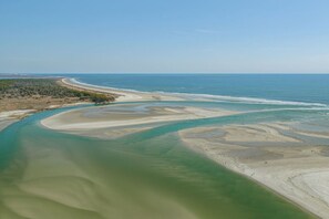 An aerial view of a coastal area with a sandy beach, a river or estuary with varying water colors, and a distant shoreline. - Sea La Vie Villa 3BD Beach Retreat Fence Yard (North Myrtle Beach)
