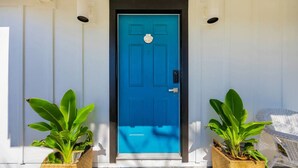 A blue door with a white doorbell, flanked by two potted plants on either side. - Sea La Vie Villa 3BD Beach Retreat Fence Yard (North Myrtle Beach)