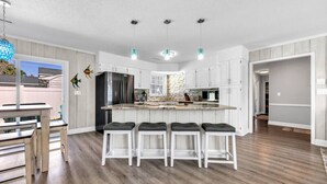 A modern kitchen with white cabinetry, a central island with bar stools, and pendant lighting. - Sea La Vie Villa 3BD Beach Retreat Fence Yard (North Myrtle Beach)