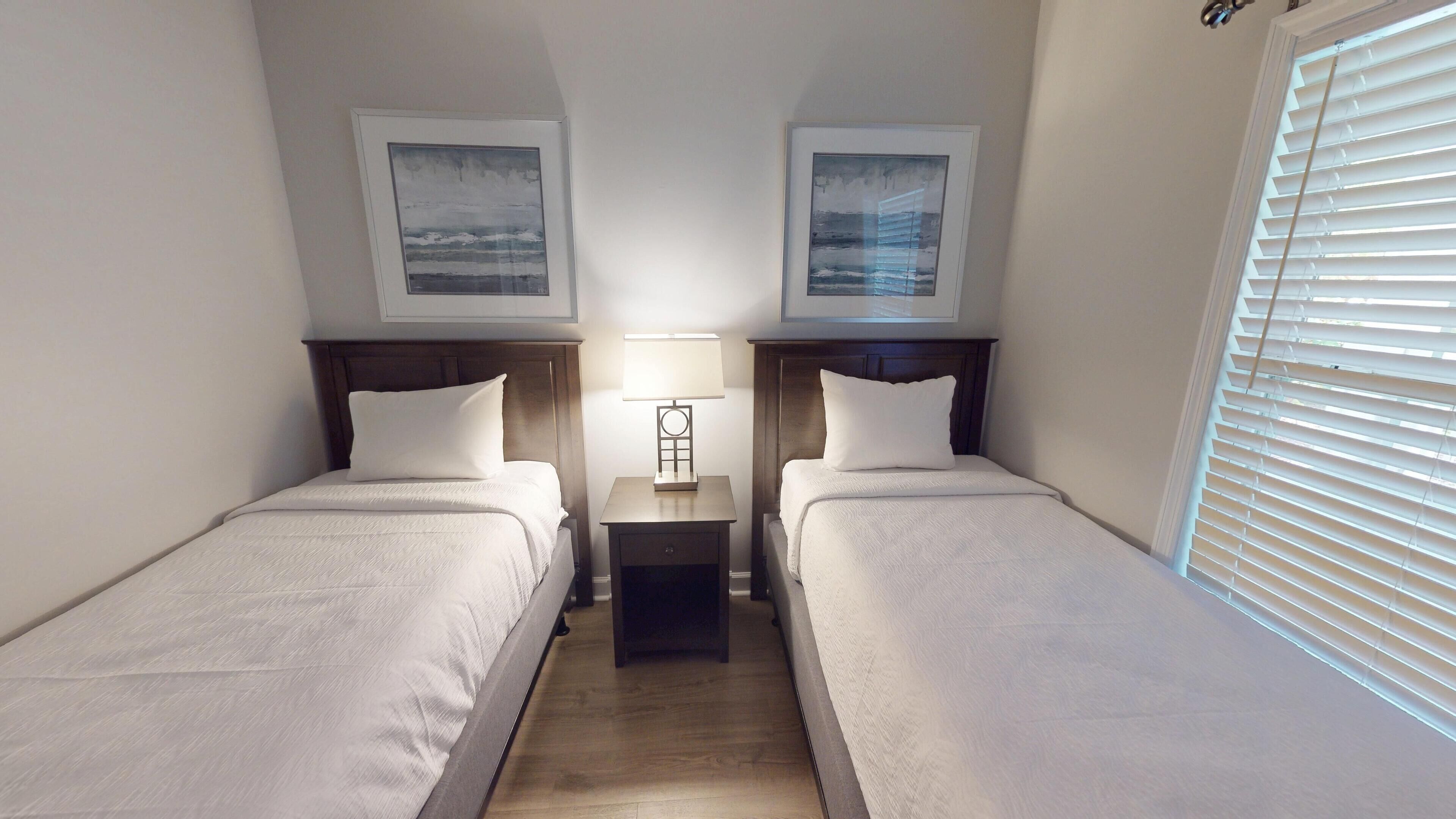A twin room with two beds, a nightstand with a lamp, and framed pictures on the walls.