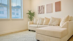 Un salon avec un canapé d’angle beige, une plante en pot et trois œuvres d’art abstraites accrochées au mur.