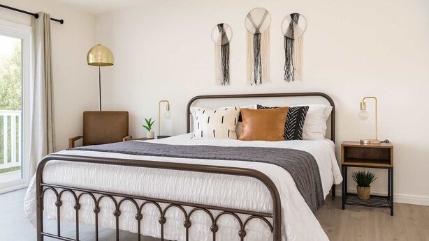 A modern bedroom with a metal bed frame, a bedside table with a lamp, and decorative wall art. - Marbella Lane - 4BR Alluring Home (Union City)