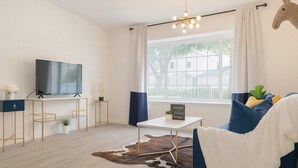 A modern living room with a flat-screen TV, a coffee table, a sofa, and a large window with curtains. - Marbella Lane - 4BR Alluring Home (Union City)