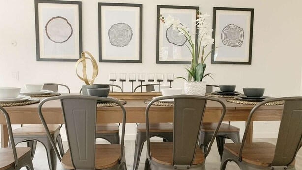 Un comedor con una mesa de madera, sillas de metal y cuadros en la pared.