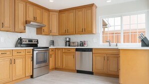 A kitchen with wooden cabinets, a stainless steel oven, a dishwasher, and a window with a view of a wooden fence. - Marbella Lane - 4BR Alluring Home (Union City)