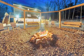 A fire pit surrounded by chairs and a wooden bench in a covered outdoor area with a building in the background. - 6 Bedrooms + Hot Tub + Game Room + Movie Theater (Hawley)