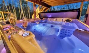 A hot tub with a wooden deck and glass railings, surrounded by trees. - 6 Bedrooms + Hot Tub + Game Room + Movie Theater (Hawley)