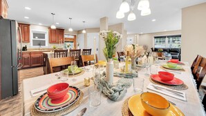 A dining area with a long table set for a meal, surrounded by wooden cabinets and a kitchen in the background. - 6 Bedrooms + Hot Tub + Game Room + Movie Theater (Hawley)