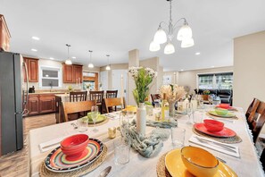 A dining area with a long table set for a meal, surrounded by wooden cabinets and a kitchen in the background. - 6 Bedrooms + Hot Tub + Game Room + Movie Theater (Hawley)