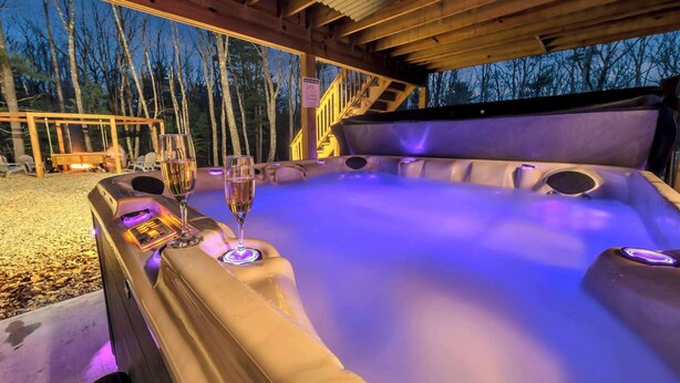 A hot tub with two glasses of champagne, surrounded by a wooden deck and a view of trees. - 6 Bedrooms + Hot Tub + Game Room + Movie Theater (Hawley)
