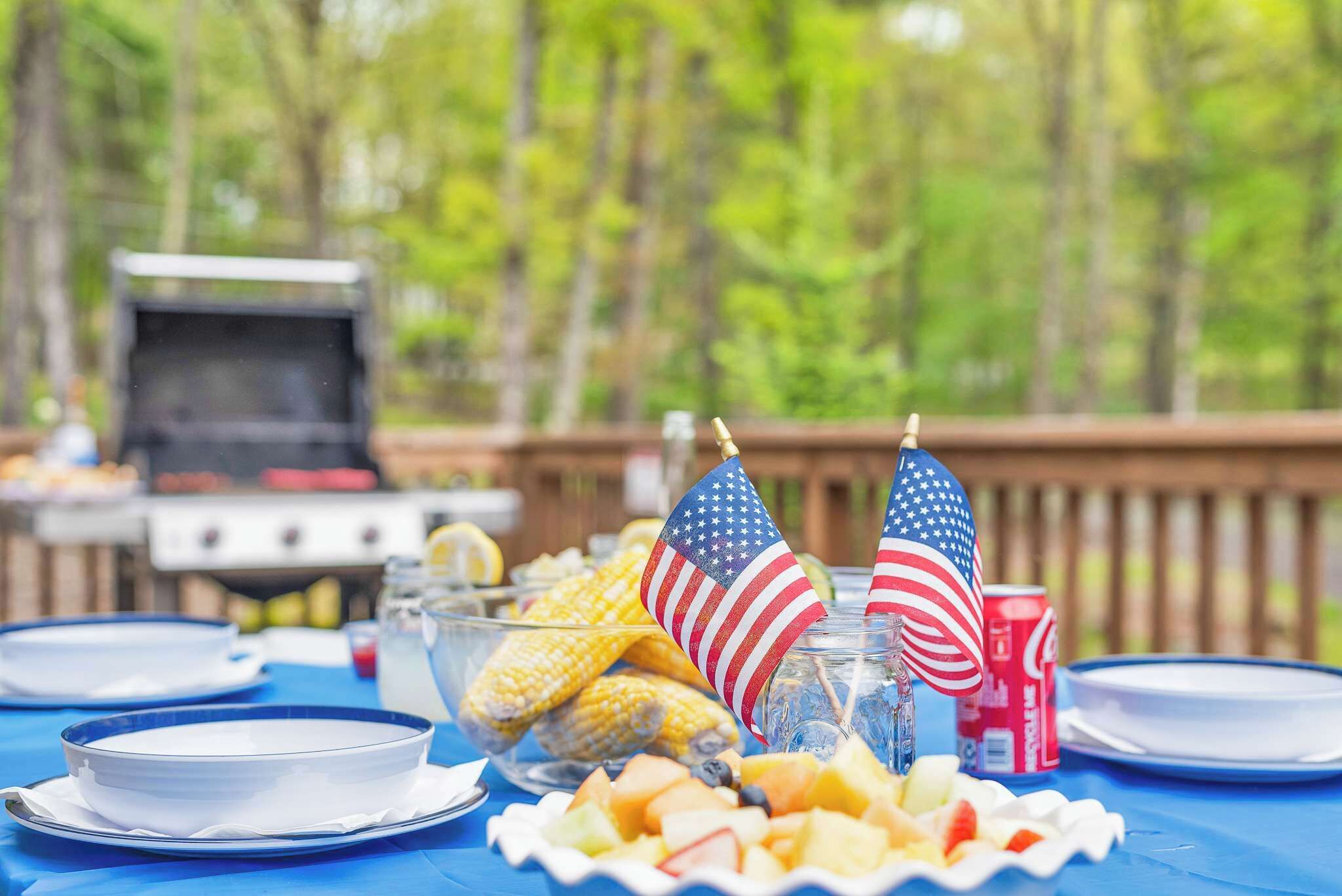 A barbecue setup with food items and American flags on a blue tablecloth.