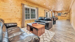 A cozy cabin interior with a leather sofa, a wooden coffee table, and a large window. - 6 Bedrooms + Hot Tub + Game Room + Movie Theater (Hawley)