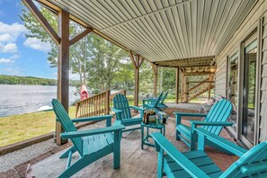 Ein überdachter Außenbereich mit Adirondack-Stühlen und einem Grill, mit Blick auf einen See.