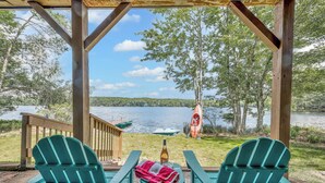 En träveranda med två gröna Adirondack-stolar, en flaska och en filt. En träräcke och en flagga syns i bakgrunden.