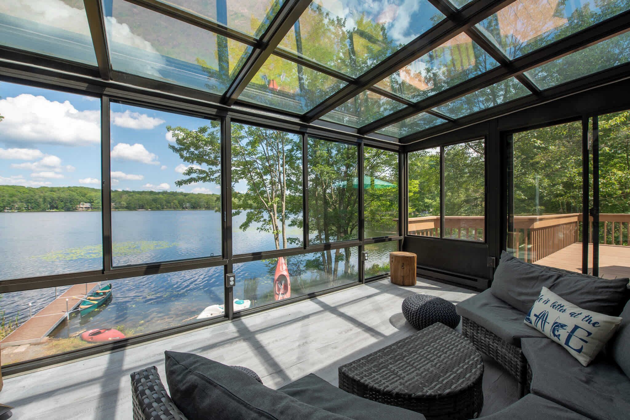 Una habitación amplia con ventanas grandes que dan a un lago, amueblada con un sofá y una pequeña mesa.