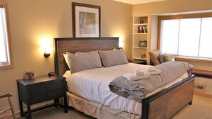A bedroom with a large bed, bedside tables, a nightstand, a bookshelf, and a window with blinds. - Lone Eagle Landing 2 (Bend)