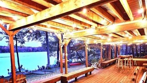 A wooden deck with benches and tables, overlooking a body of water. - Lakefront Hot Tub Canoes Game Room Wood FP (Gouldsboro)