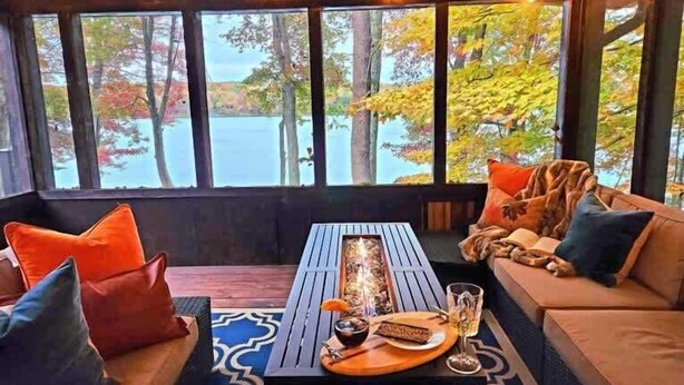 A cozy room with a wooden ceiling, large windows, a wooden table with a tray, and a sofa with cushions. - Lakefront Hot Tub Canoes Game Room Wood FP (Gouldsboro)