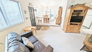 A living room with a leather sofa, a wooden TV stand, and a dining area with a table and chairs. - Timber 12 (Bend)