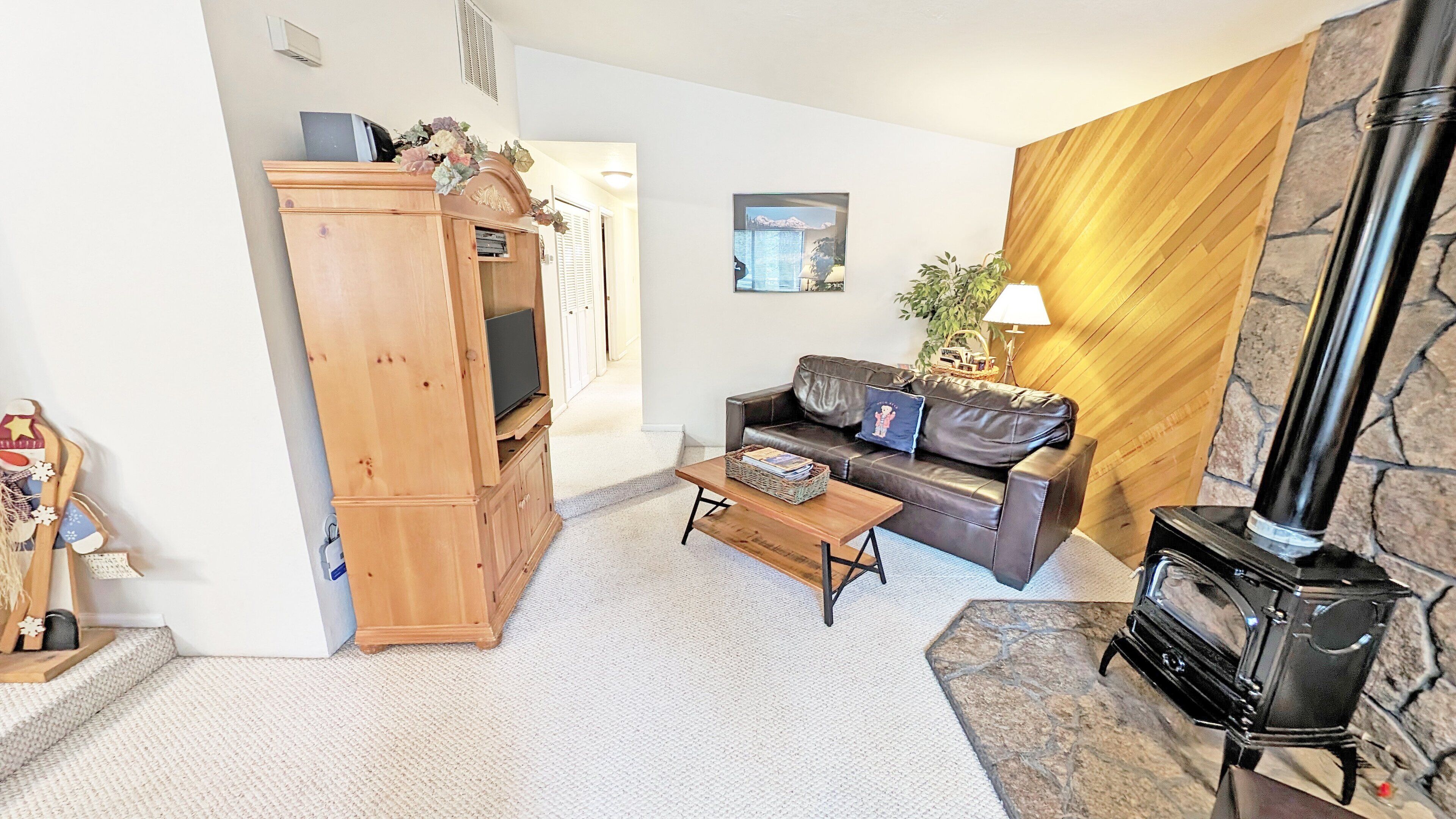 A living room with a wooden entertainment center, a leather sofa, a coffee table, a fireplace, and a stone accent wall.