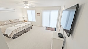 A bedroom with a bed, a ceiling fan, a TV, and large windows. - Timber 12 (Bend)