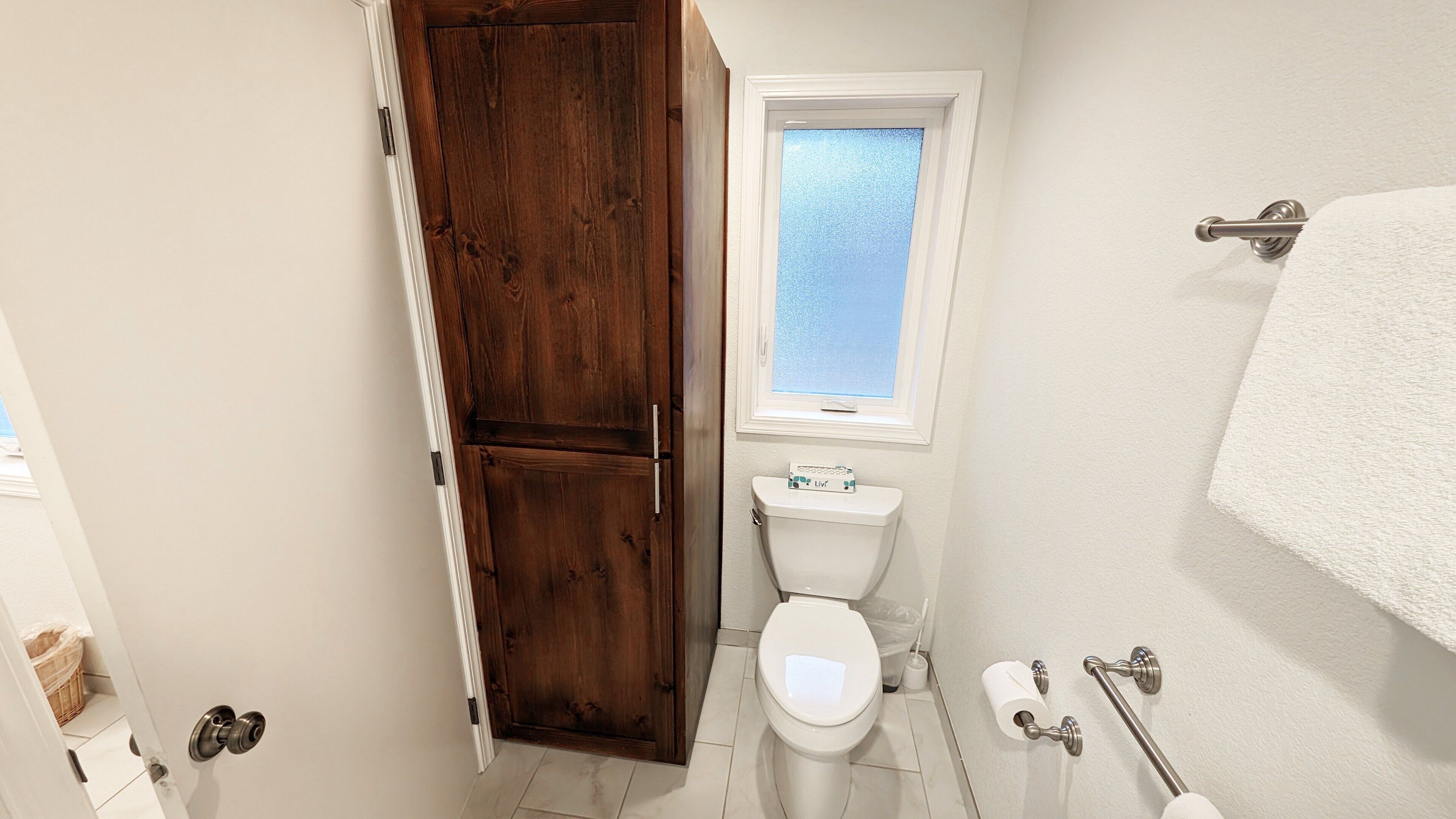 A bathroom with a toilet, a wooden cabinet, a window, and a towel rack.