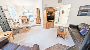 A living room with a sofa, a TV stand, a dining area with chairs, and a staircase. - Timber 12 (Bend)