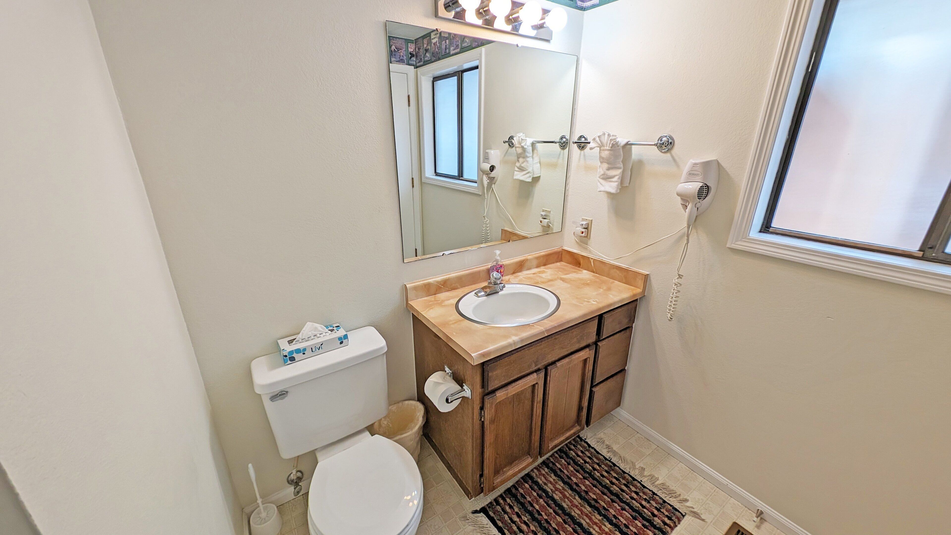 Un baño con inodoro, lavamanos, espejo, toallero y ventana.