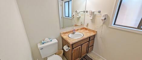 Un baño con inodoro, lavamanos, espejo, toallero y ventana.