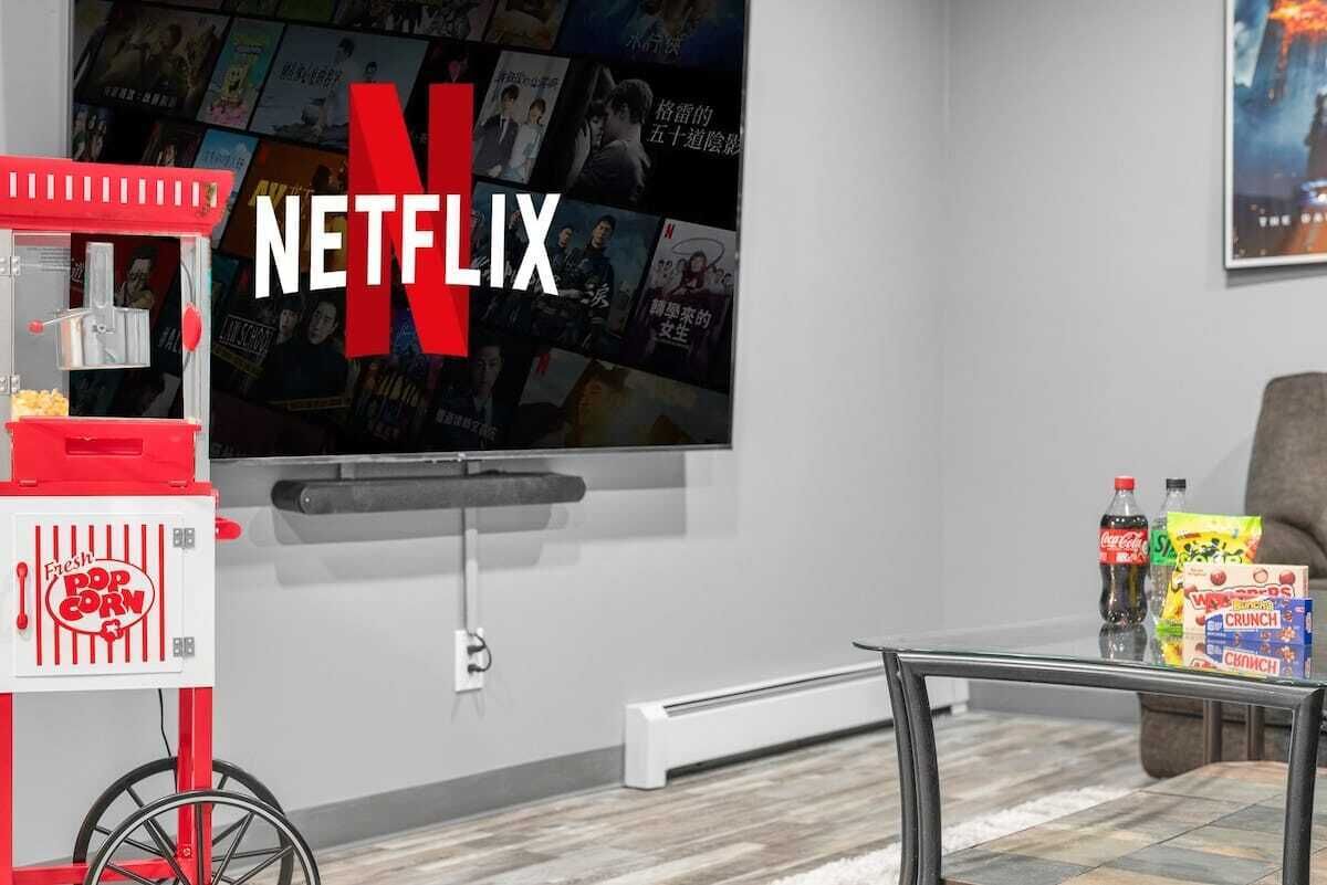 Ein Wohnzimmer mit einem großen Flachbildfernseher an der Wand, einem Popcornewagen und einem Glastisch.
