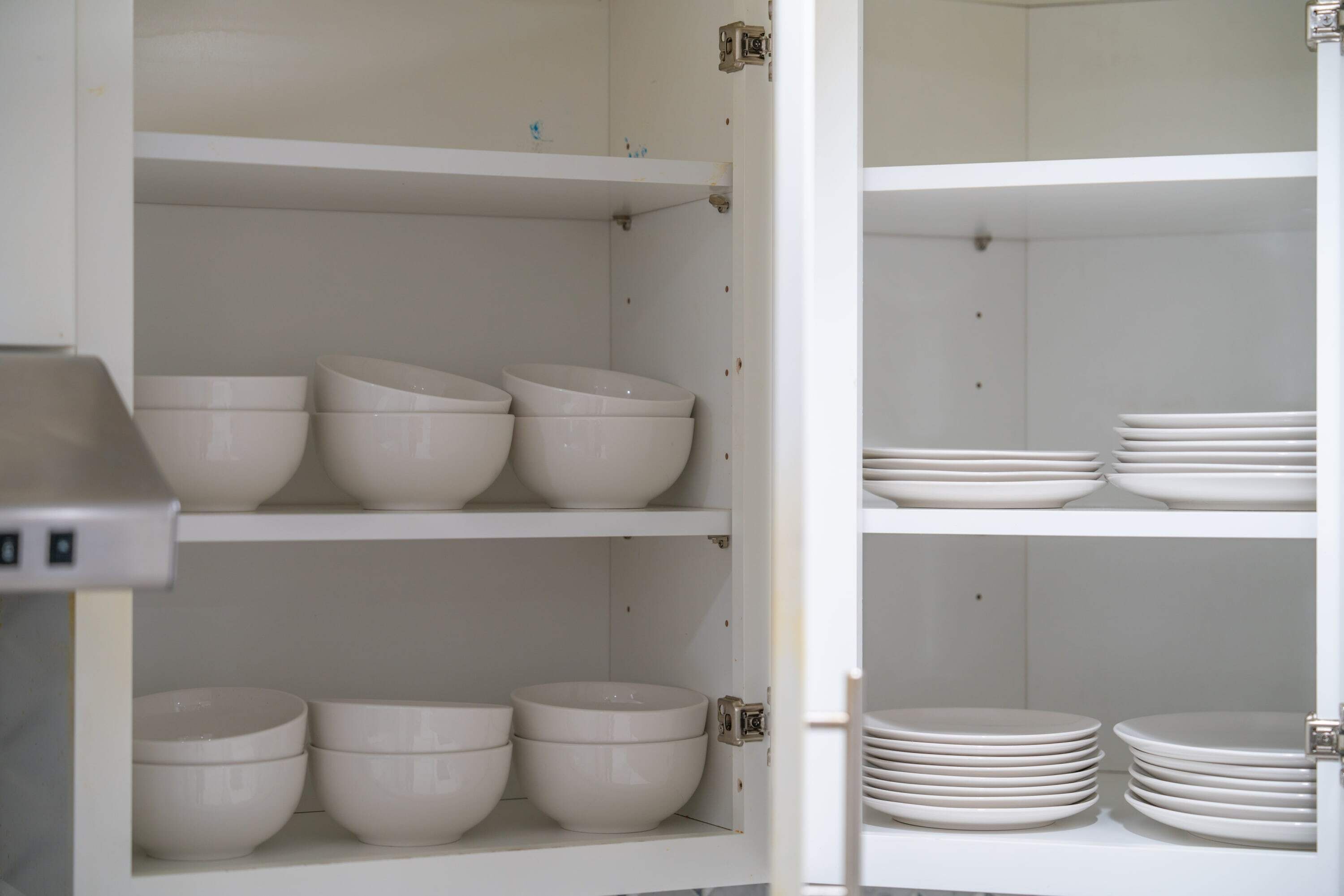 A kitchen cabinet with white shelves holding bowls and plates.