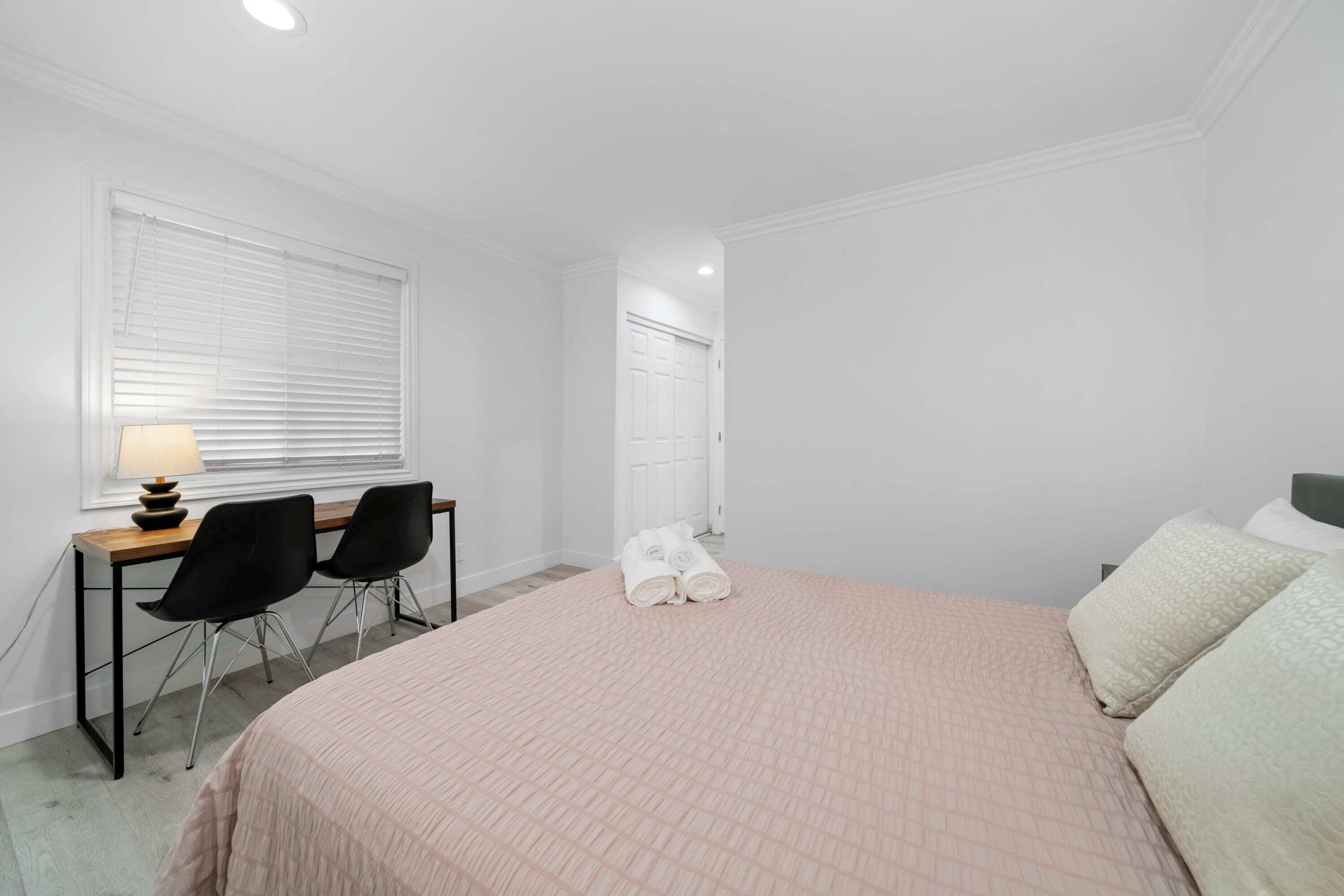 A bedroom with a bed, a desk with two chairs, a lamp, and a door.