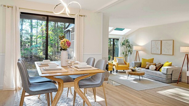 A modern living room with a dining area, featuring a large window, a sofa set, and a dining table with chairs.