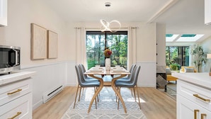 A modern dining area with a large window, a dining table set for four, and a kitchen with white cabinetry and a microwave.