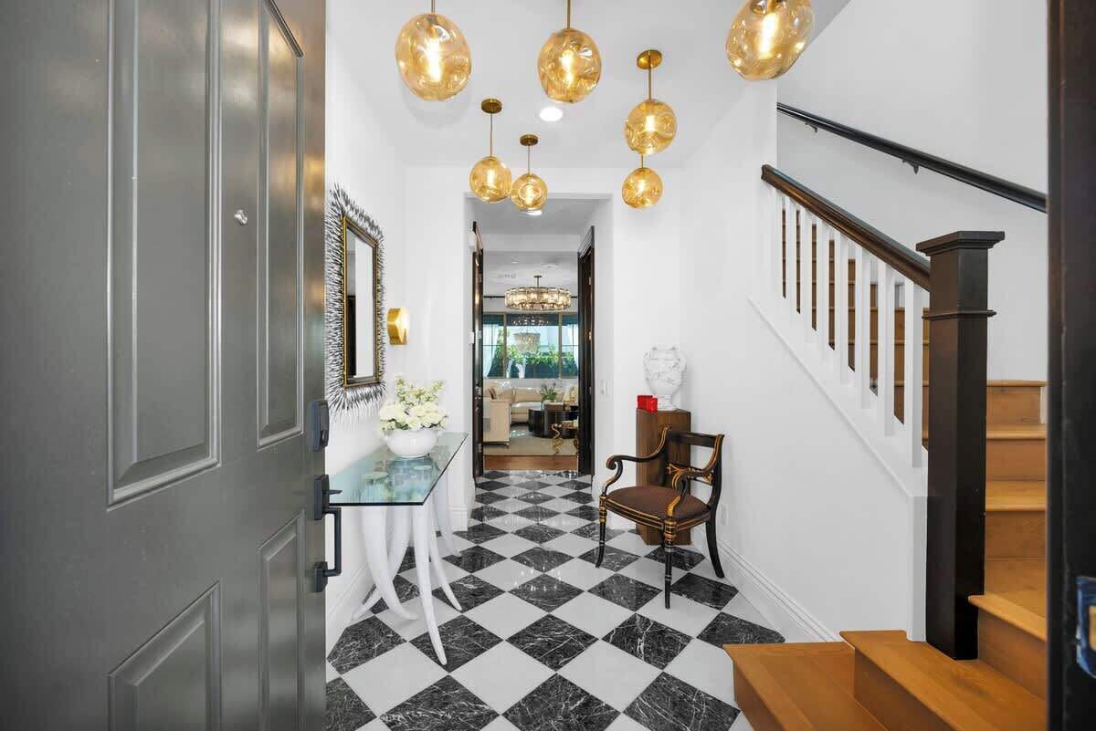 Un couloir doté d’un sol à carreaux, une table en verre avec un vase, une chaise et un escalier muni d’une rampe.