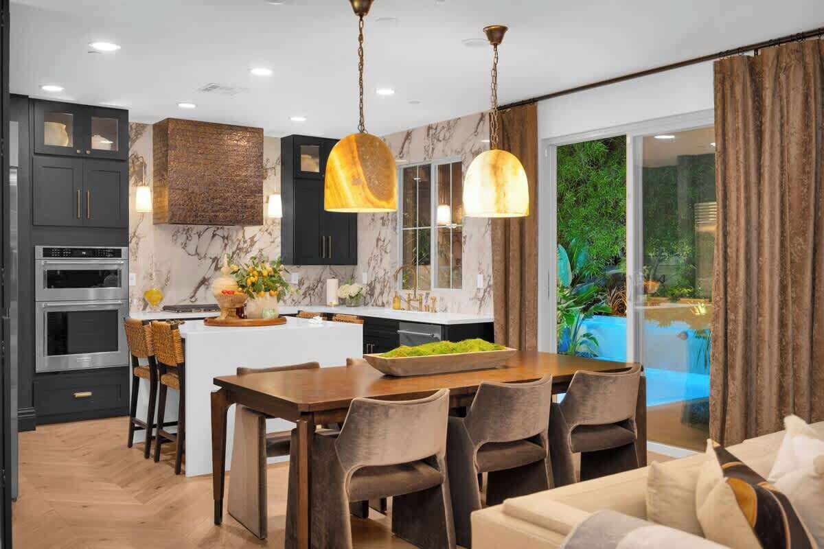 A modern kitchen with dark cabinets, a marble backsplash, and pendant lighting.