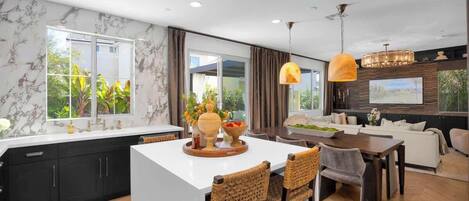 Une cuisine moderne dotée d’un îlot central, de meubles de couleur sombre et d’un coin repas avec des chaises en osier et une table en bois.