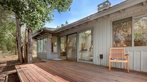 Terraza de madera con banco, puertas correderas grandes de vidrio y pared exterior blanca.