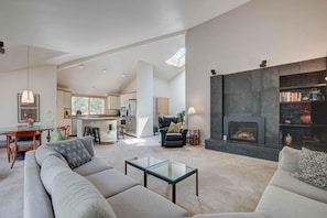 A spacious living area with a fireplace, a sofa, a coffee table, and a kitchen in the background. - Rocky Mountain 4 (Bend)
