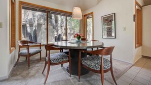 Un comedor con una mesa redonda, cuatro sillas, un florero con flores y una lámpara colgante.