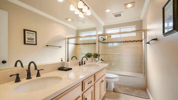 Un baño con lavamanos doble, un espejo grande, cabina de ducha de vidrio y un inodoro.