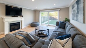 A modern living room with a fireplace, a large flat-screen TV, a sectional sofa, and a sliding glass door leading to a backyard. - @ Marbella Lane - Seaside Retreat Laundry + P (Half Moon Bay)