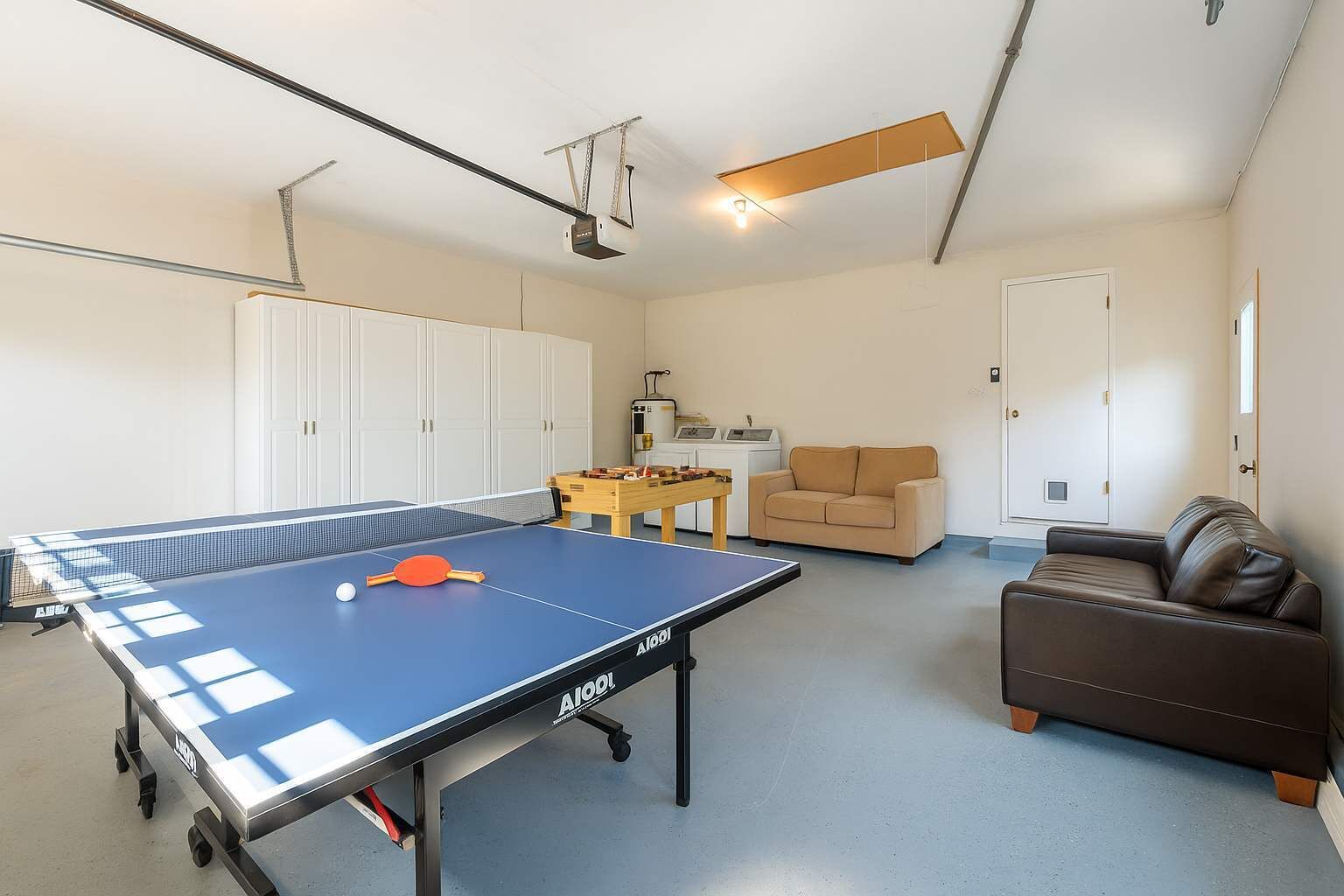A spacious room with a ping pong table, a sofa, a coffee table, and a cabinet.