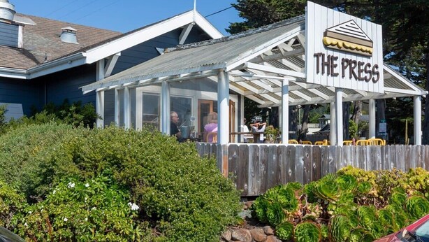 A building with a sign reading "THE PRESS" and a covered outdoor seating area. - @ Marbella Lane - Seaside Retreat Laundry + P (Half Moon Bay)