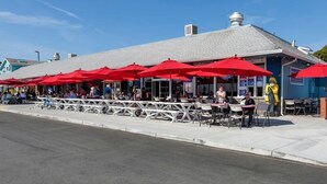 An outdoor seating area with red umbrellas, white tables, and chairs, and a building with a grey roof. - @ Marbella Lane - Seaside Retreat Laundry + P (Half Moon Bay)