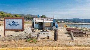 A beachside kayak rental station with a sign for Half Moon Bay Kayak Co., picnic tables, and a view of the ocean. - @ Marbella Lane - Seaside Retreat Laundry + P (Half Moon Bay)