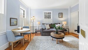 A living room with a round wooden table, two grey upholstered chairs, a grey sofa with patterned cushions, a woven side table, and a patterned rug. - The Royce on Spring - High-end Family Getaway in Newport (Newport)